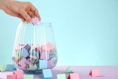 Photo of Woman taking violet paper piece from glass jar on color background, closeup. Space for text