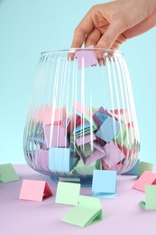 Photo of Woman taking violet paper piece from glass jar on color background, closeup