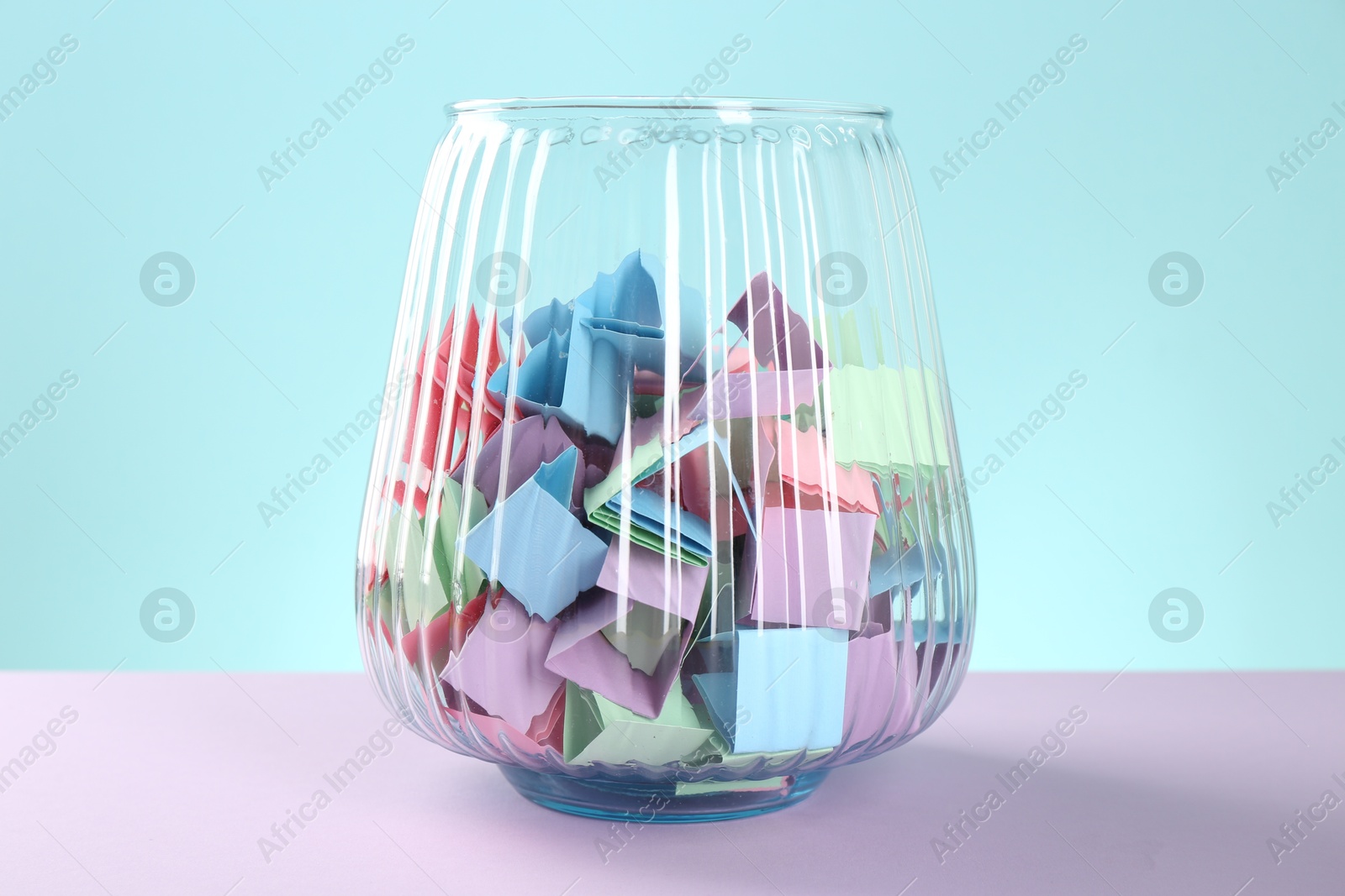 Bright paper pieces in glass jar on color background, closeup Photo of Bright paper pieces in glass jar on color background, closeup