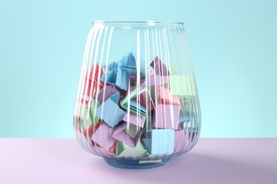 Photo of Bright paper pieces in glass jar on color background, closeup