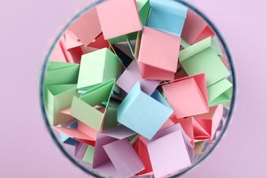 Photo of Colorful paper pieces in glass jar on violet background, top view