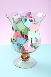 Photo of Bright paper pieces in glass jar on color background, closeup