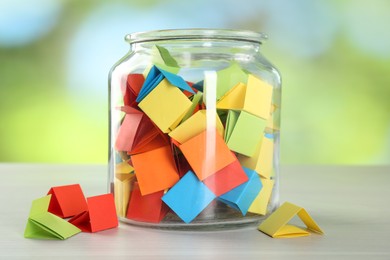 Photo of Colorful paper pieces in glass jar on wooden table against blurred background, closeup