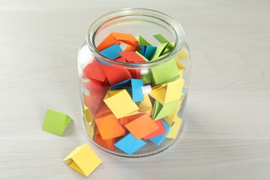 Photo of Colorful paper pieces in glass jar on wooden table, closeup