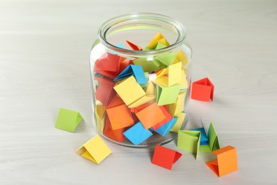 Photo of Colorful paper pieces in glass jar on wooden table, closeup