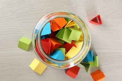 Photo of Colorful paper pieces in glass jar on wooden table, top view
