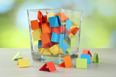 Photo of Colorful paper pieces in glass jar on wooden table against blurred background, closeup