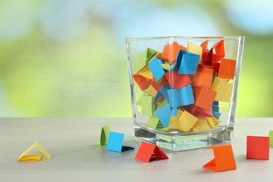 Photo of Colorful paper pieces in glass jar on wooden table against blurred background. Space for text