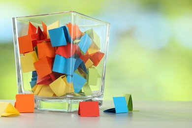 Photo of Colorful paper pieces in glass jar on wooden table against blurred background, closeup. Space for text