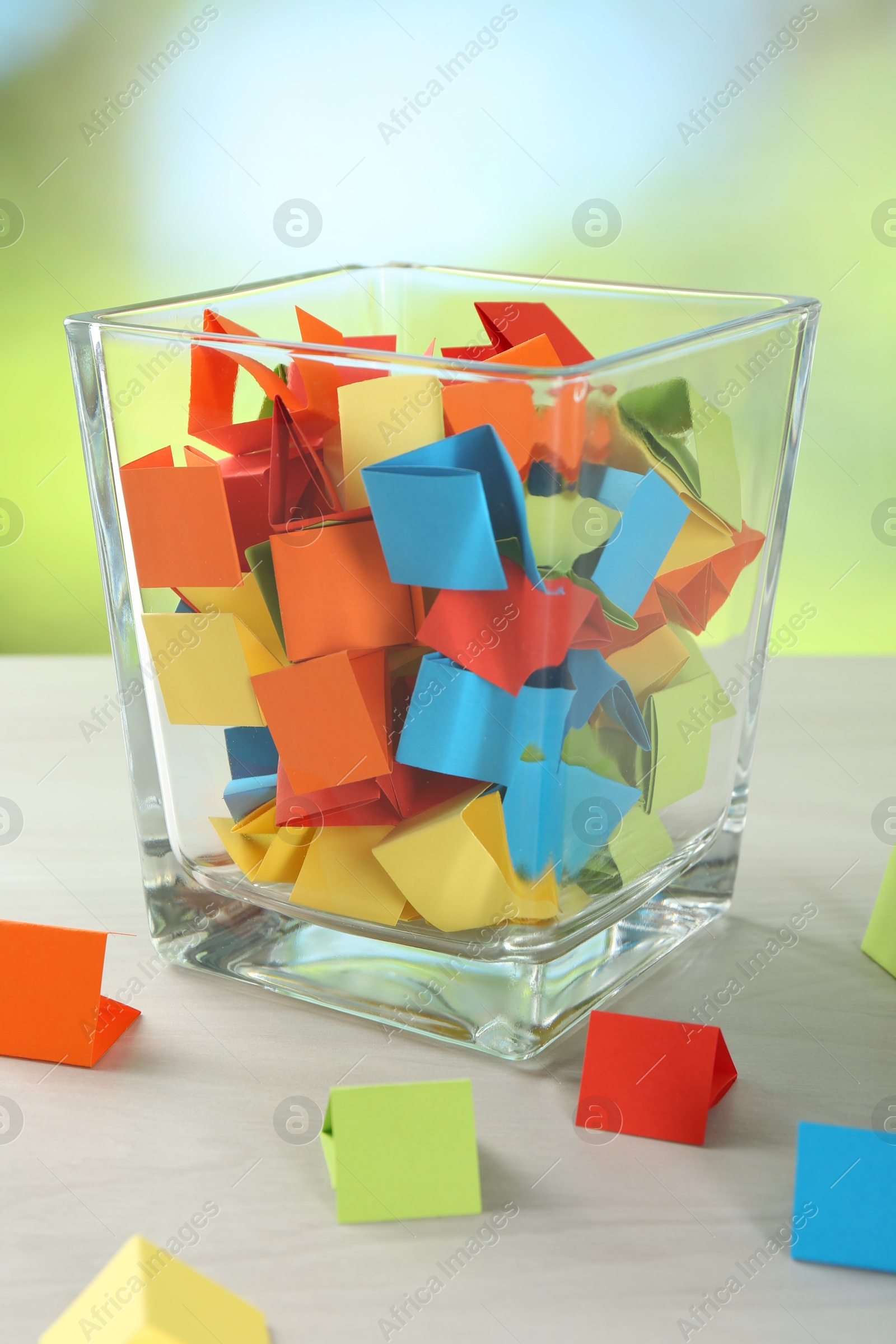 Colorful paper pieces in glass jar on wooden table against blurred background, closeup Photo of Colorful paper pieces in glass jar on wooden table against blurred background, closeup
