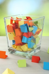 Photo of Colorful paper pieces in glass jar on wooden table against blurred background, closeup