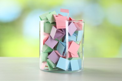 Photo of Colorful paper pieces in glass jar on wooden table against blurred background