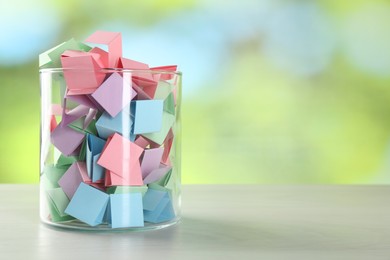 Photo of Colorful paper pieces in glass jar on wooden table against blurred background. Space for text