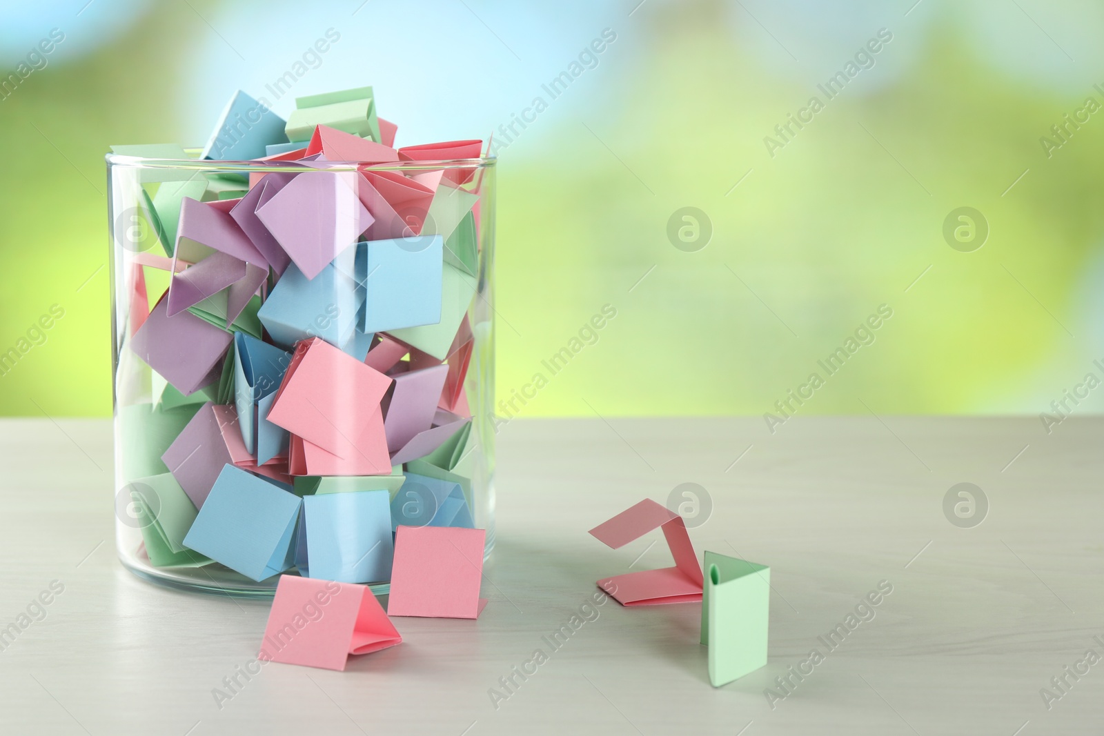 Colorful paper pieces in glass jar on wooden table against blurred background. Space for text Photo of Colorful paper pieces in glass jar on wooden table against blurred background. Space for text