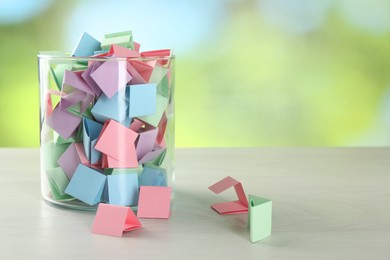 Photo of Colorful paper pieces in glass jar on wooden table against blurred background. Space for text