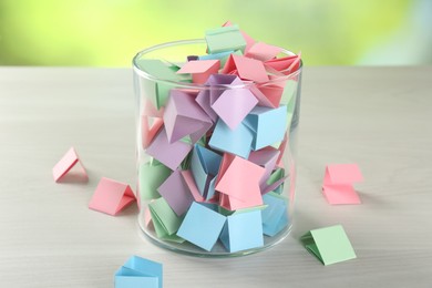 Photo of Colorful paper pieces in glass jar on wooden table, closeup