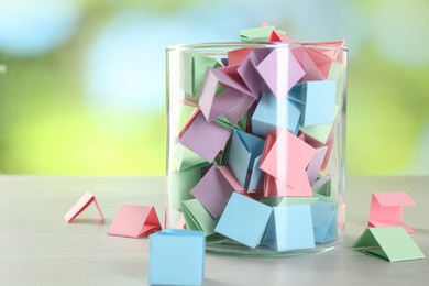 Photo of Colorful paper pieces in glass jar on wooden table against blurred background, closeup