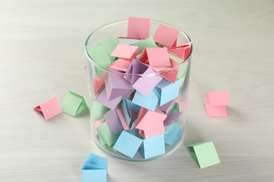 Photo of Colorful paper pieces in glass jar on wooden table, closeup