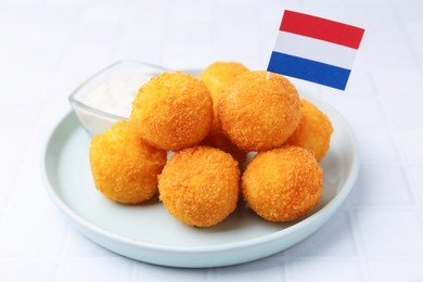 Photo of Delicious fried croquette balls and flag of Netherlands on light tiled table, closeup