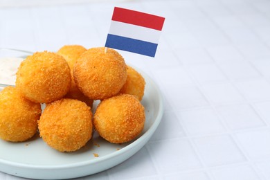 Photo of Delicious fried croquette balls and flag of Netherlands on light tiled table, closeup. Space for text