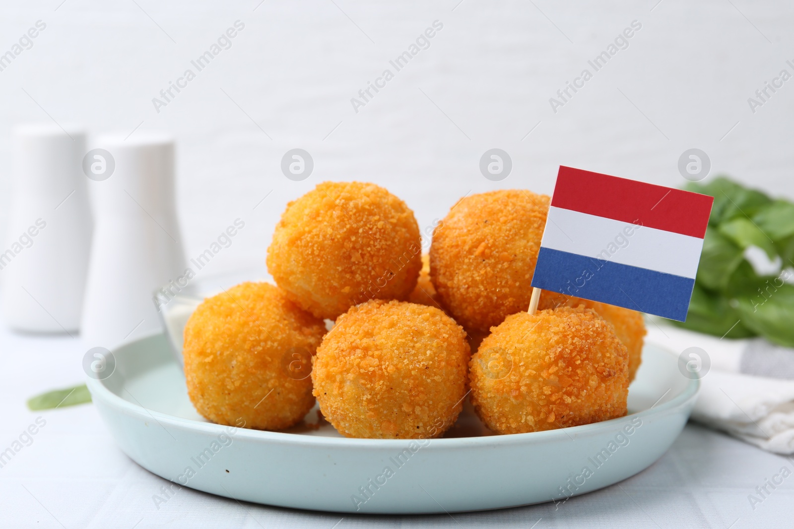 Photo of Delicious fried croquette balls and flag of Netherlands on light table, closeup