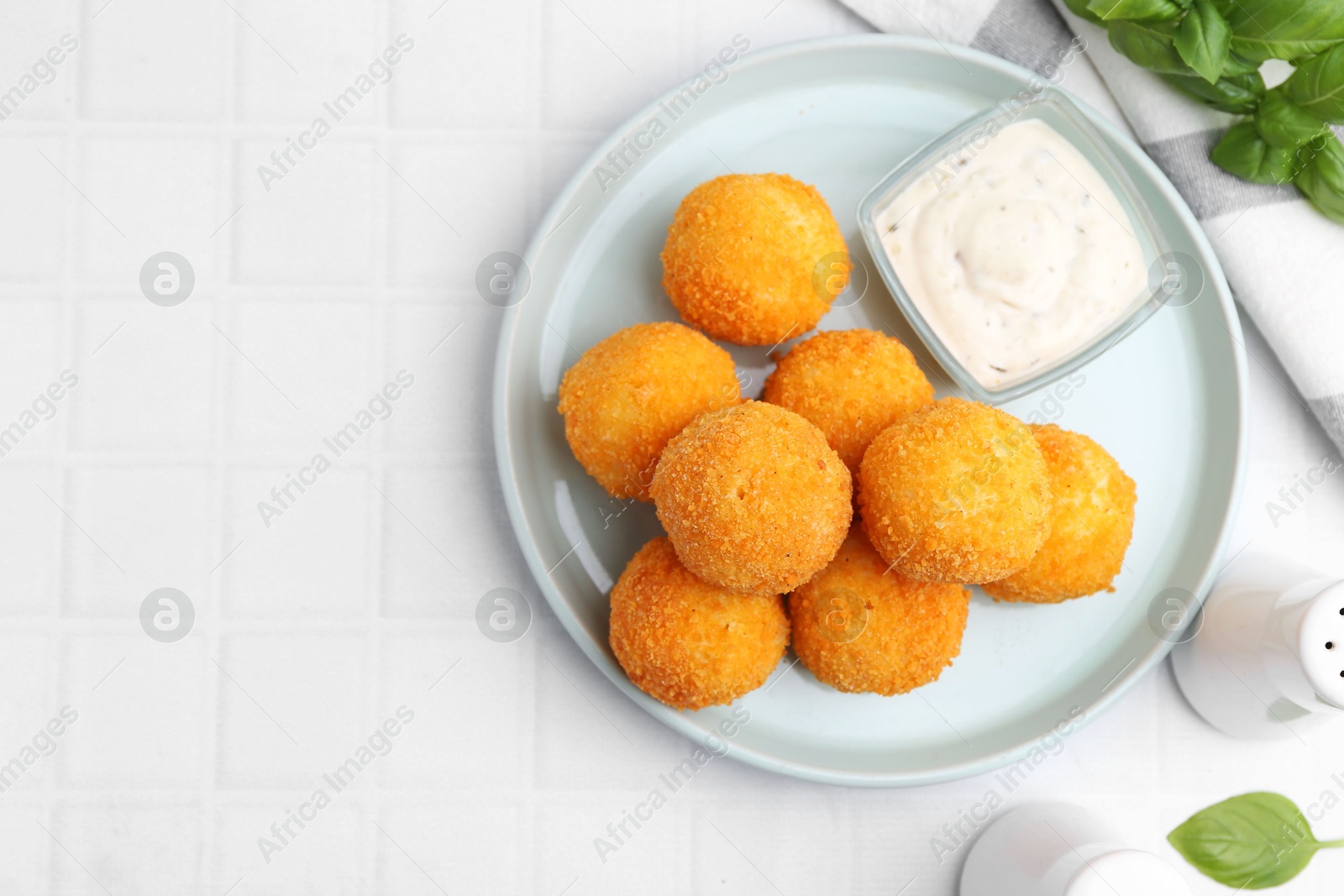 Photo of Delicious fried croquette balls, sauce and basil on light tiled table, flat lay. Space for text