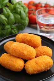 Photo of Delicious fried croquettes, glass of water, tomatoes and basil on table, closeup