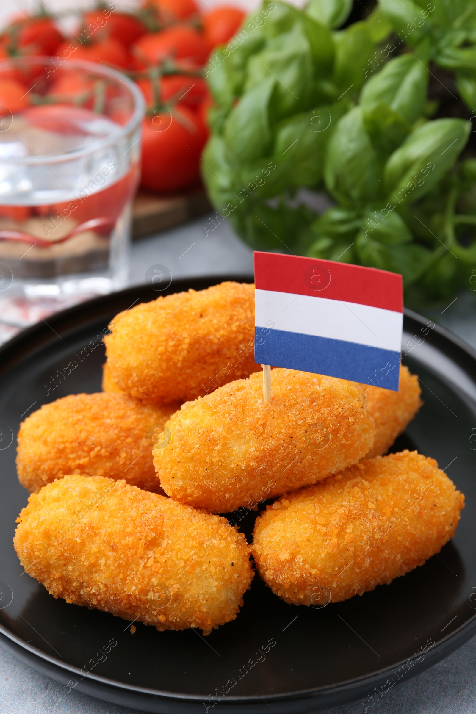 Delicious fried croquettes, flag of Netherlands, water, tomatoes and basil on table, closeup Photo of Delicious fried croquettes, flag of Netherlands, water, tomatoes and basil on table, closeup