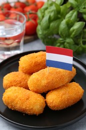 Photo of Delicious fried croquettes, flag of Netherlands, water, tomatoes and basil on table, closeup