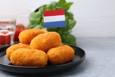 Photo of Delicious fried croquettes and flag of Netherlands on gray table, closeup