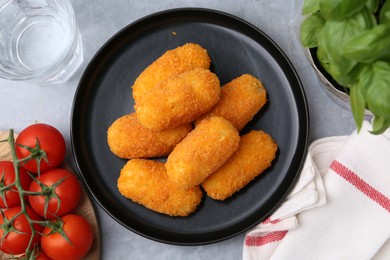 Photo of Delicious fried croquettes, glass of water, tomatoes and basil on gray table, flat lay