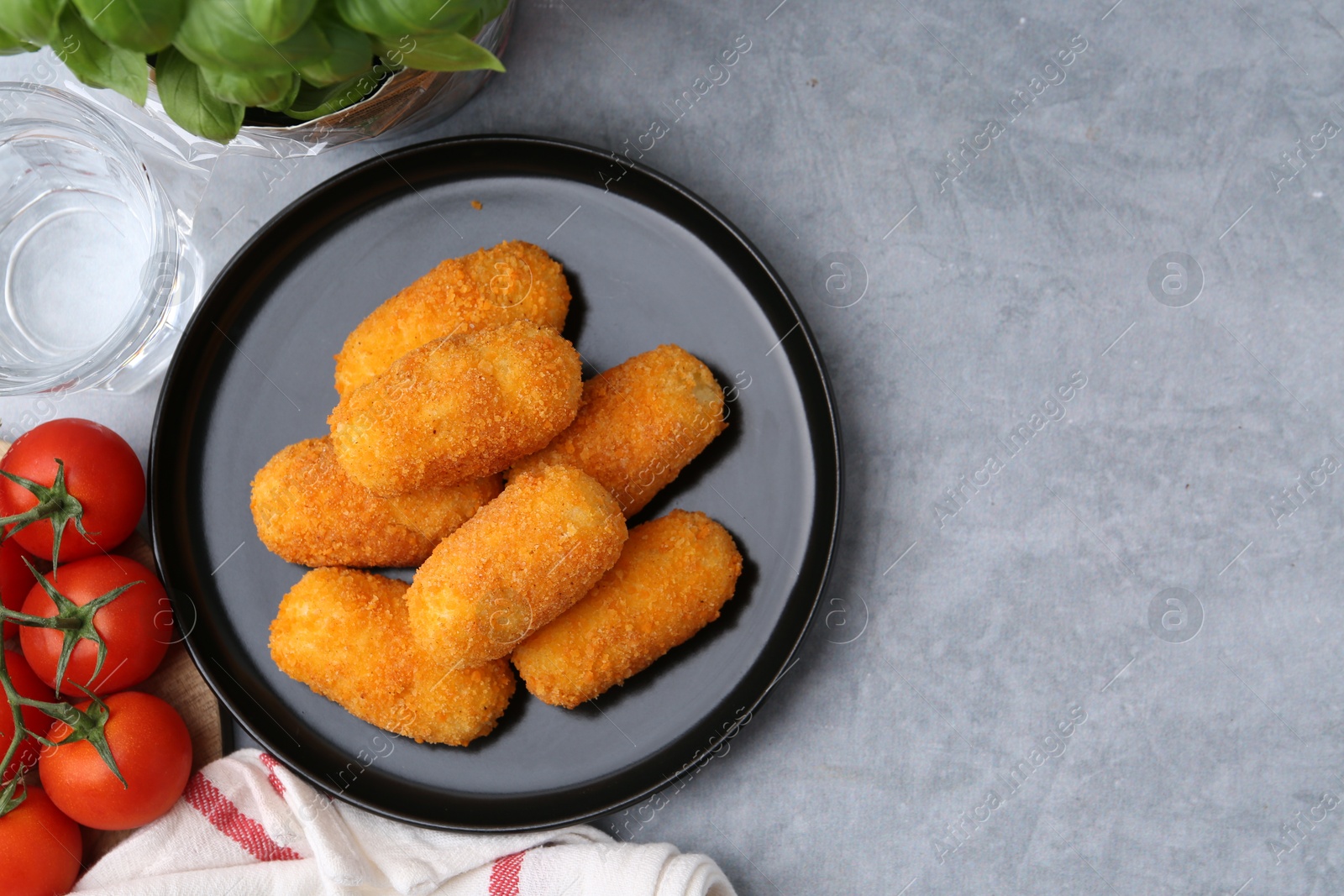 Delicious fried croquettes, glass of water, tomatoes and basil on gray textured table, flat lay. Space for text Photo of Delicious fried croquettes, glass of water, tomatoes and basil on gray textured table, flat lay. Space for text