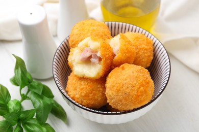 Photo of Delicious fried croquette balls in bowl and spices on white wooden table, closeup