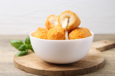 Photo of Delicious fried croquettes in bowl and basil on wooden table, closeup