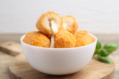 Photo of Delicious fried croquettes in bowl and basil on table, closeup