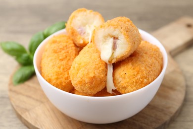 Photo of Delicious fried croquettes in bowl and basil on table, closeup
