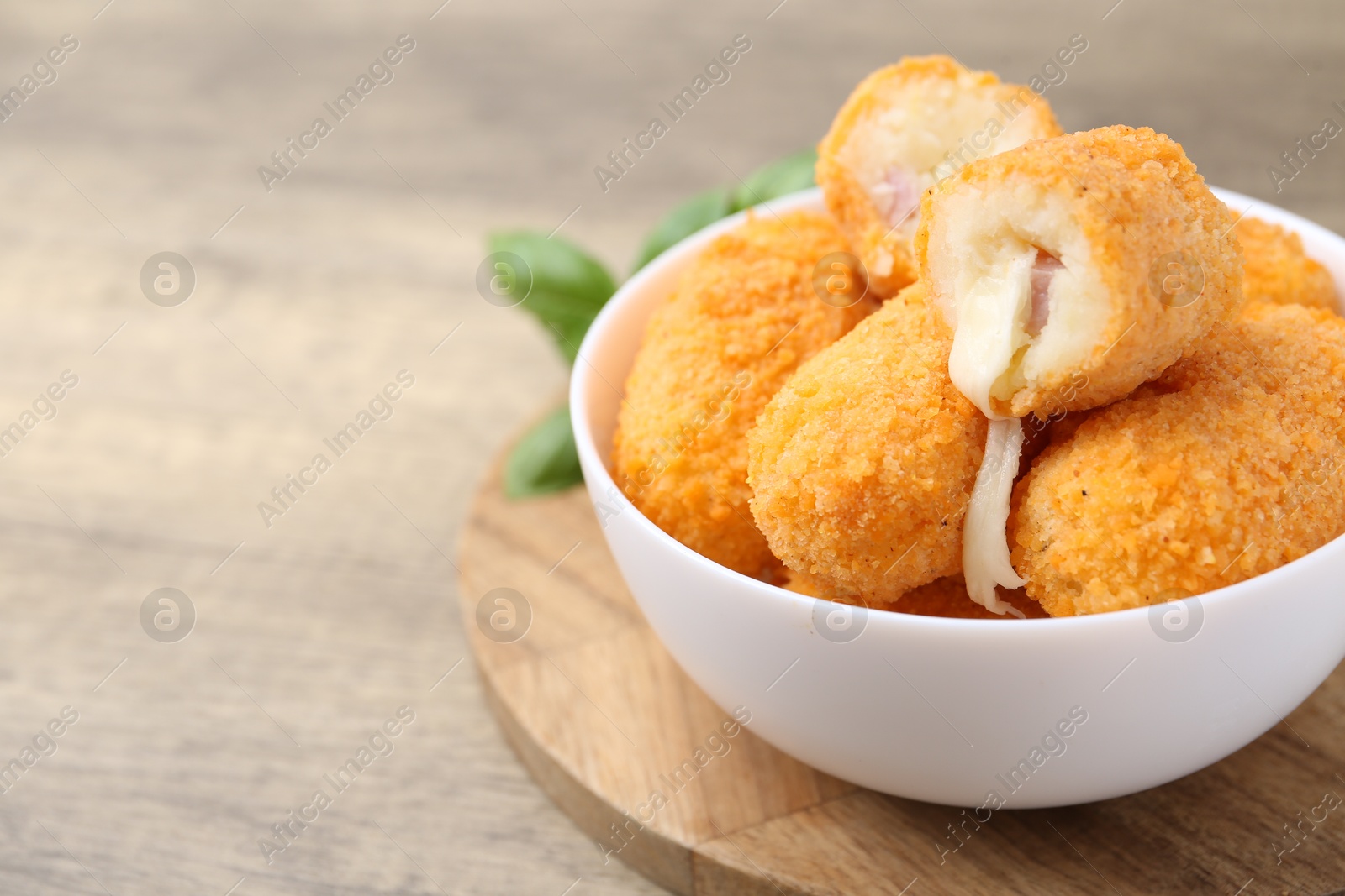 Delicious fried croquettes in bowl and basil on wooden table, closeup. Space for text Photo of Delicious fried croquettes in bowl and basil on wooden table, closeup. Space for text