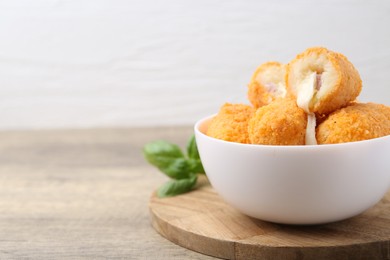 Photo of Delicious fried croquettes in bowl and basil on wooden table, closeup. Space for text