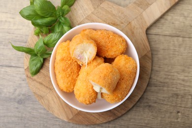 Photo of Delicious fried croquettes in bowl and basil on wooden table, flat lay
