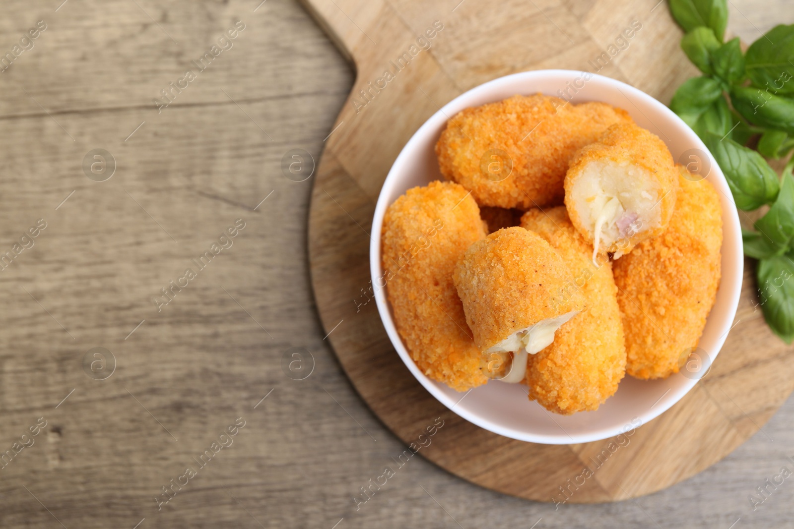 Delicious fried croquettes in bowl and basil on wooden table, flat lay. Space for text Photo of Delicious fried croquettes in bowl and basil on wooden table, flat lay. Space for text