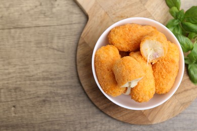 Photo of Delicious fried croquettes in bowl and basil on wooden table, flat lay. Space for text