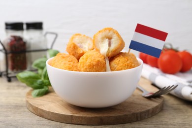 Photo of Delicious fried croquettes in bowl and flag of Netherlands on wooden table, closeup