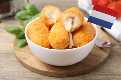 Photo of Delicious fried croquettes in bowl and flag of Netherlands on wooden table, closeup