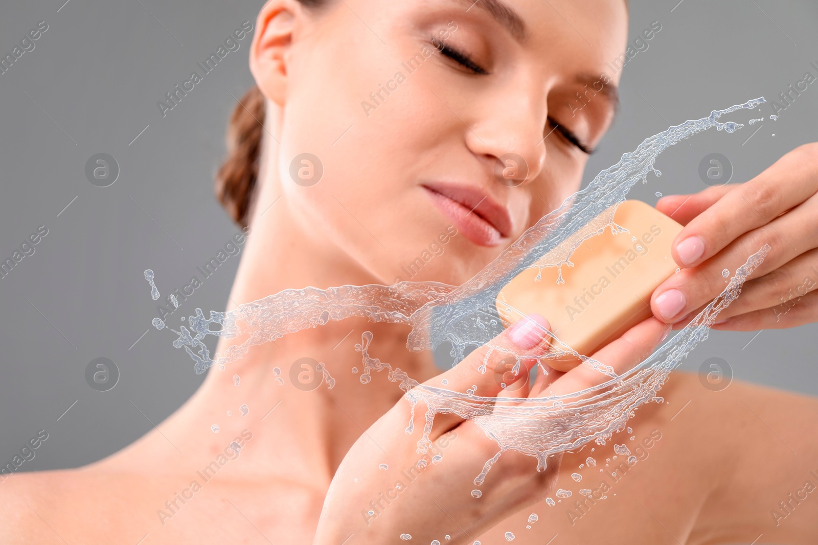 Woman washing face with soap bar and water splashes on grey background, closeup Image of Woman washing face with soap bar and water splashes on grey background, closeup