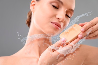 Image of Woman washing face with soap bar and water splashes on grey background, closeup