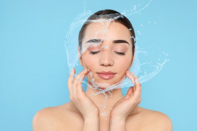 Image of Woman with smooth skin and water splashes on light blue background