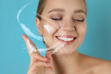 Image of Young woman washing face with cleansing foam and water splashes on light blue background