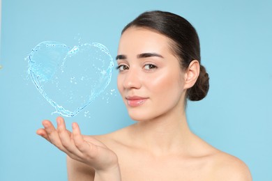 Image of Woman with smooth skin and water splash in shape of heart on light blue background
