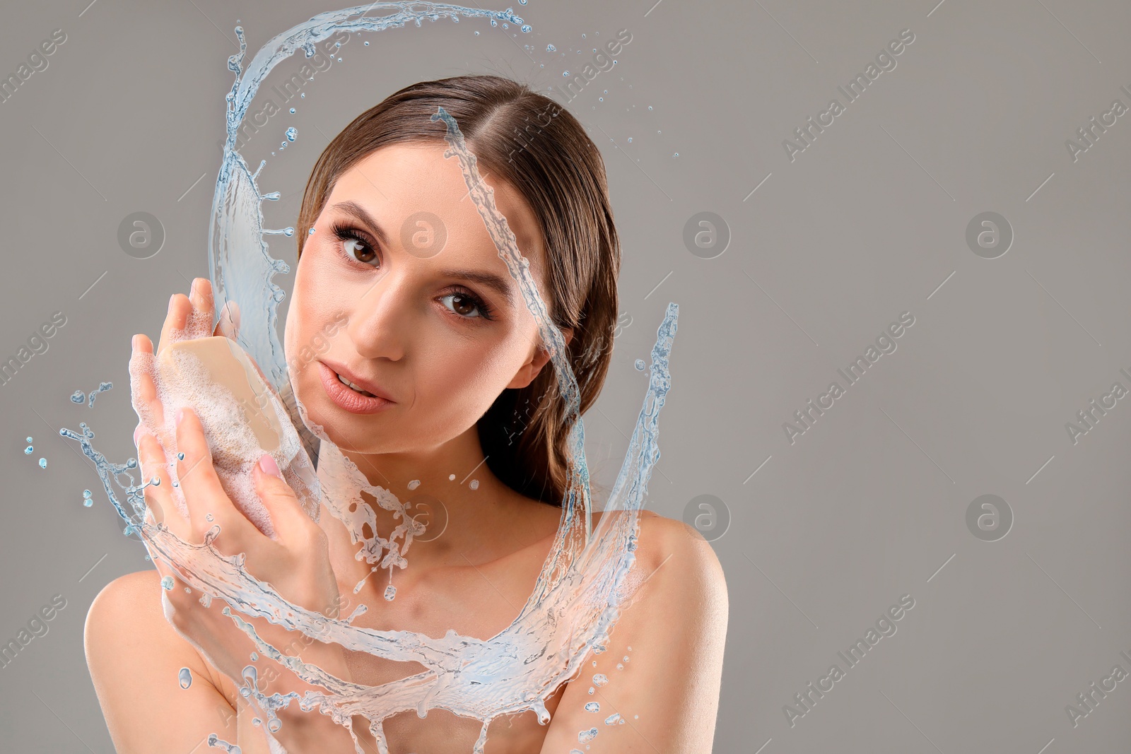 Woman washing face with soap bar and water splashes on grey background, space for text Image of Woman washing face with soap bar and water splashes on grey background, space for text