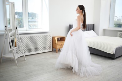 Photo of Dreams come true. Woman wearing beautiful wedding dress looking at herself in mirror indoors